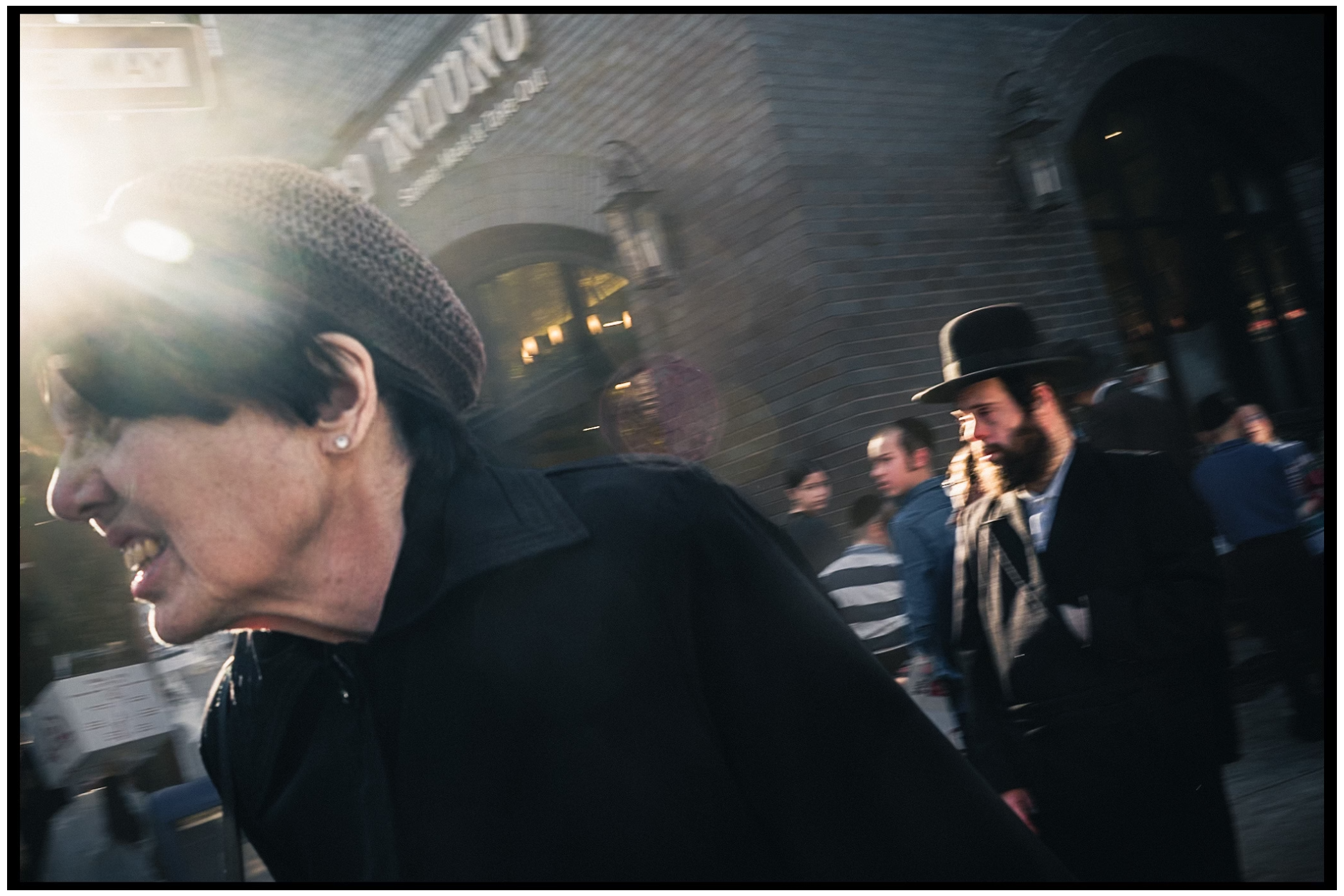 People walk through steam and city streets at dusk with shadows and glowing lights in the background. Kapparot, Brooklyn NYC