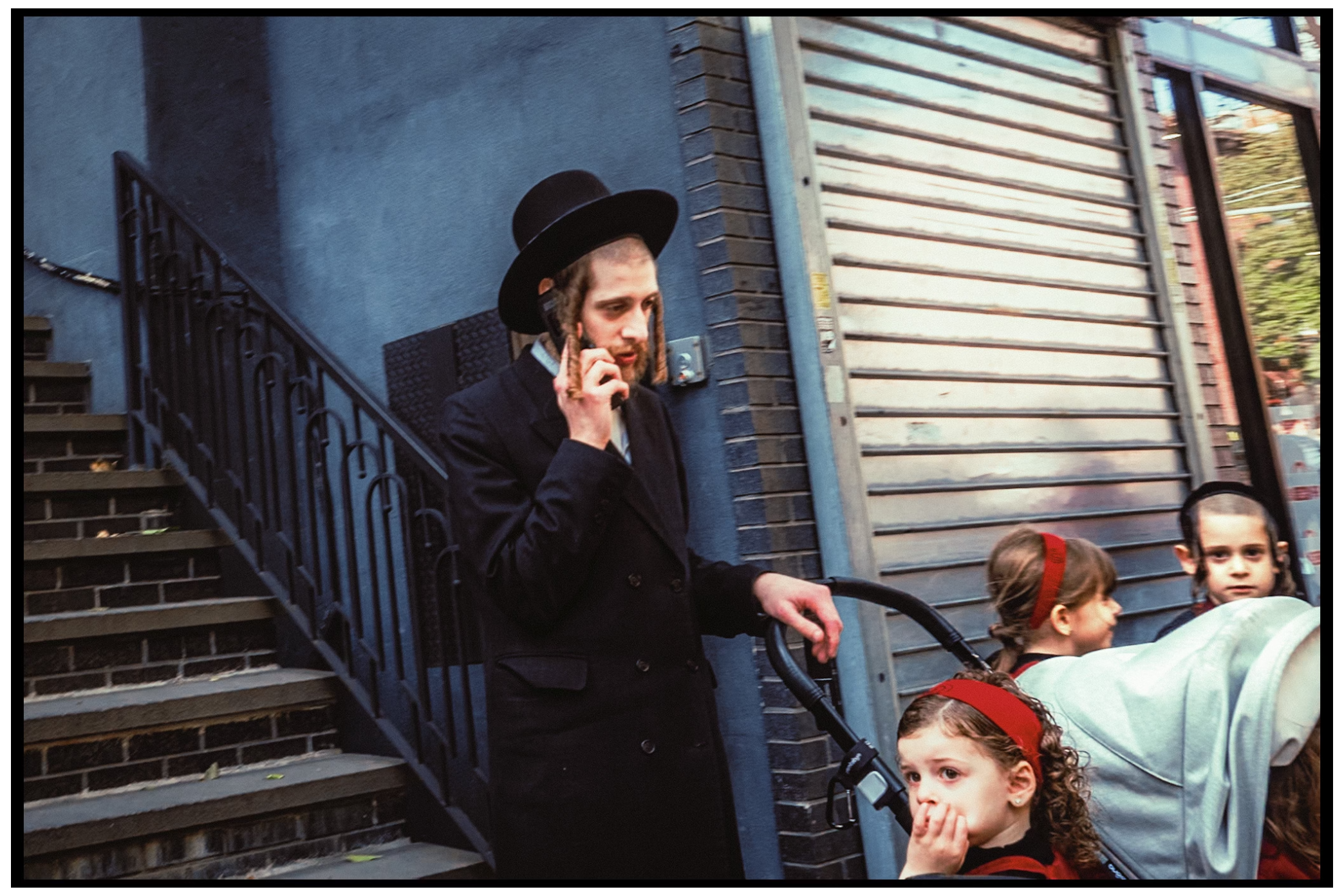 Street scene with figures standing near steps of a building at dusk. Kapparot, Brooklyn NYC