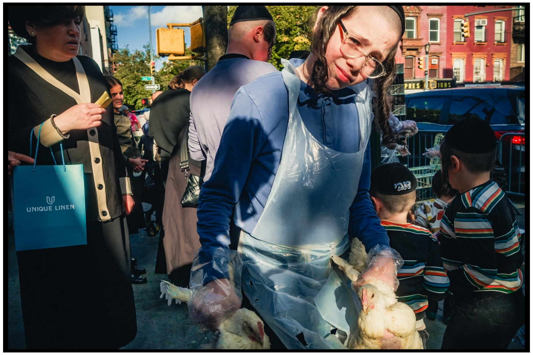 Urban street photography showing people gathered outside on a sunny day. Kapparot, Brooklyn NYC