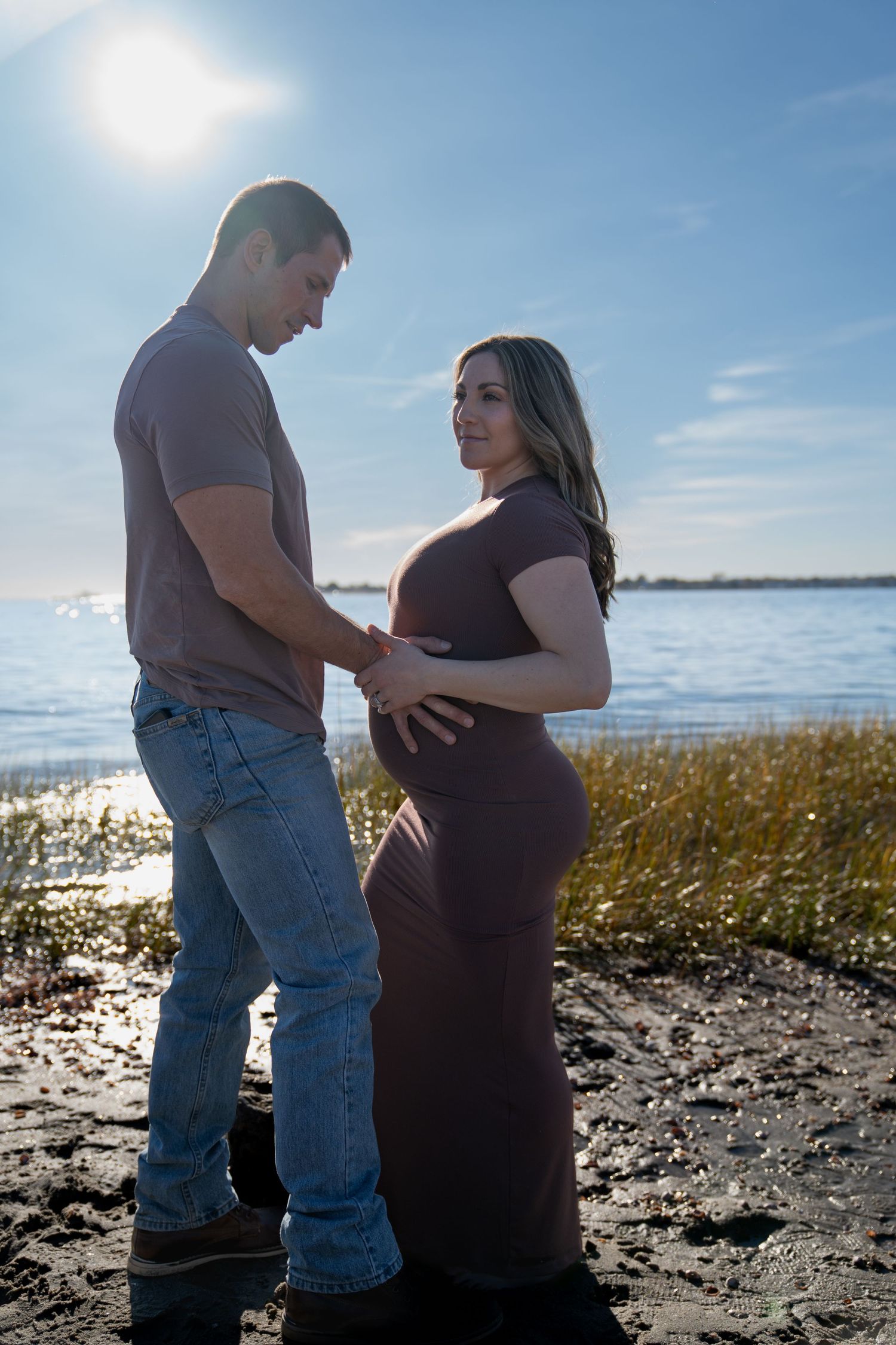 Silhouettes of a couple on a beach during sunset with a pregnant belly.