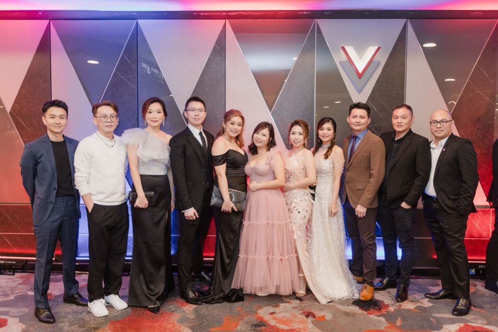 Formal group photo of attendees in evening wear posing against a modern geometric backdrop with red lighting.