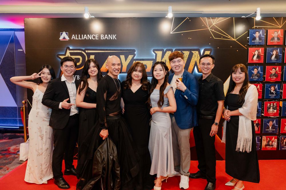Event attendees pose in formal attire against an Alliance Bank backdrop with decorative lighting.