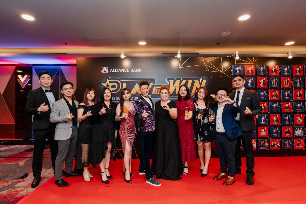 Event attendees pose together on a red carpet with corporate branding and geometric wall designs.