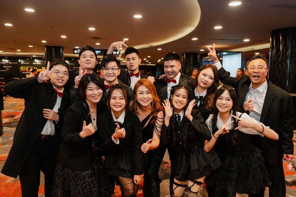 Large group celebrates together indoors making peace signs in formal black attire.