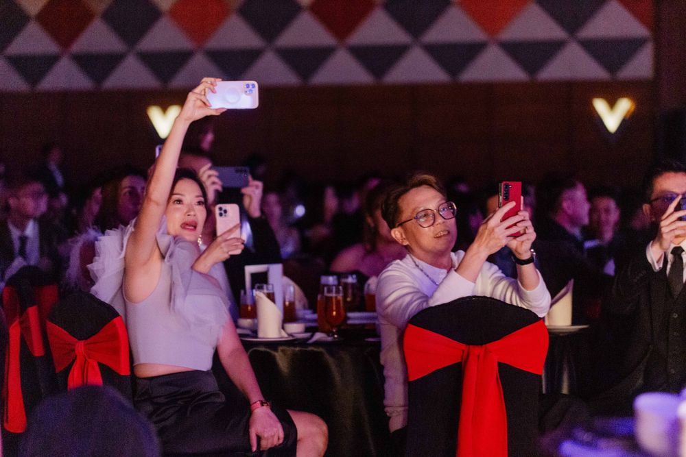 Audience members holding up phones to capture moments during an indoor event.