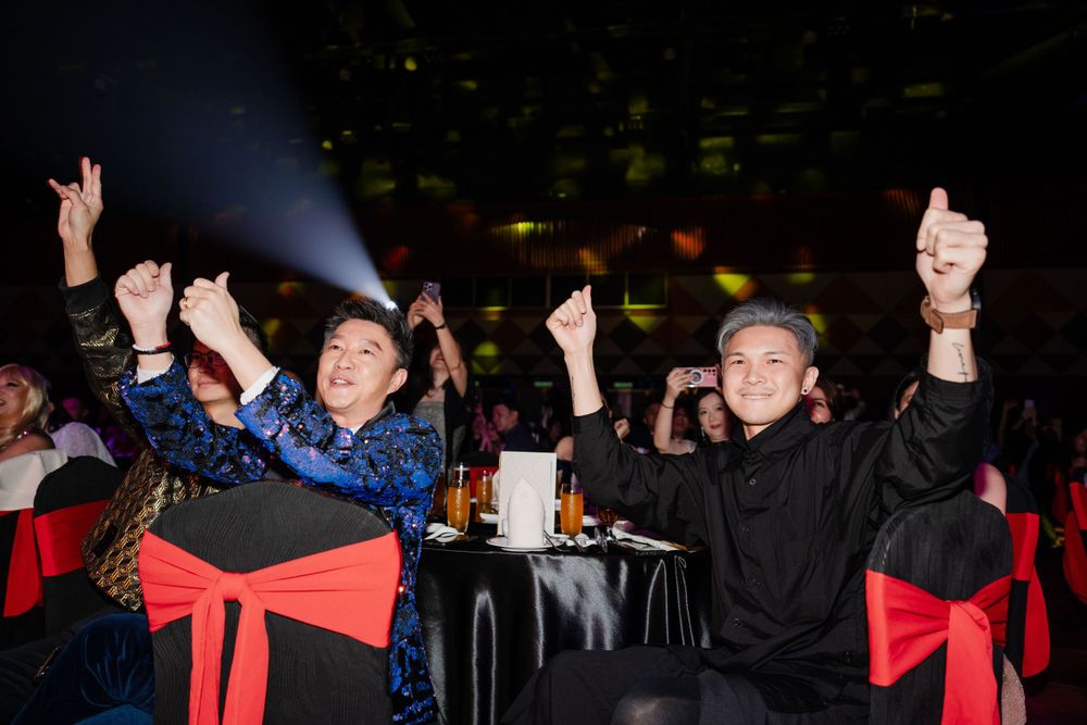Enthusiastic audience members cheering with red bow-tied chairs in a dark venue.