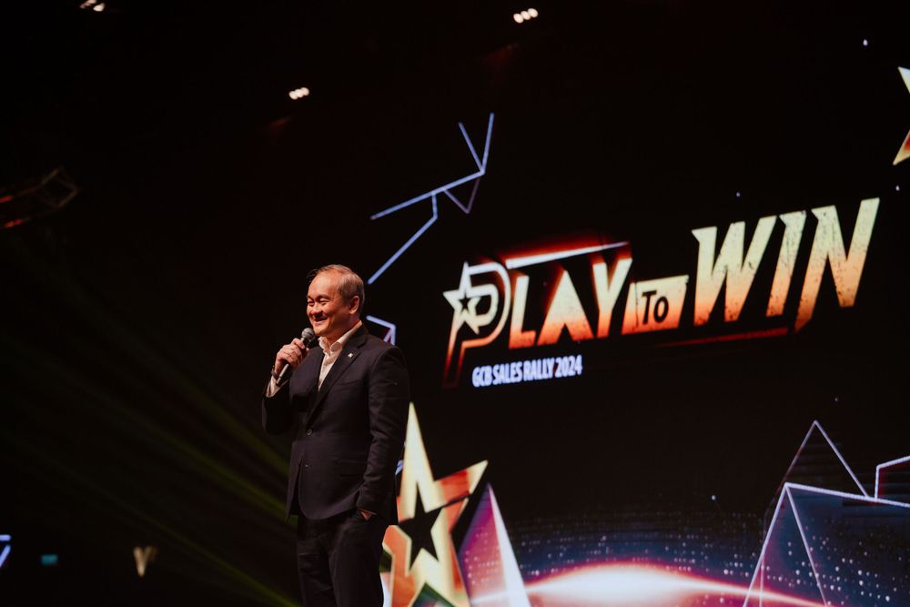 Speaker on dark stage with Play to Win text display in background.
