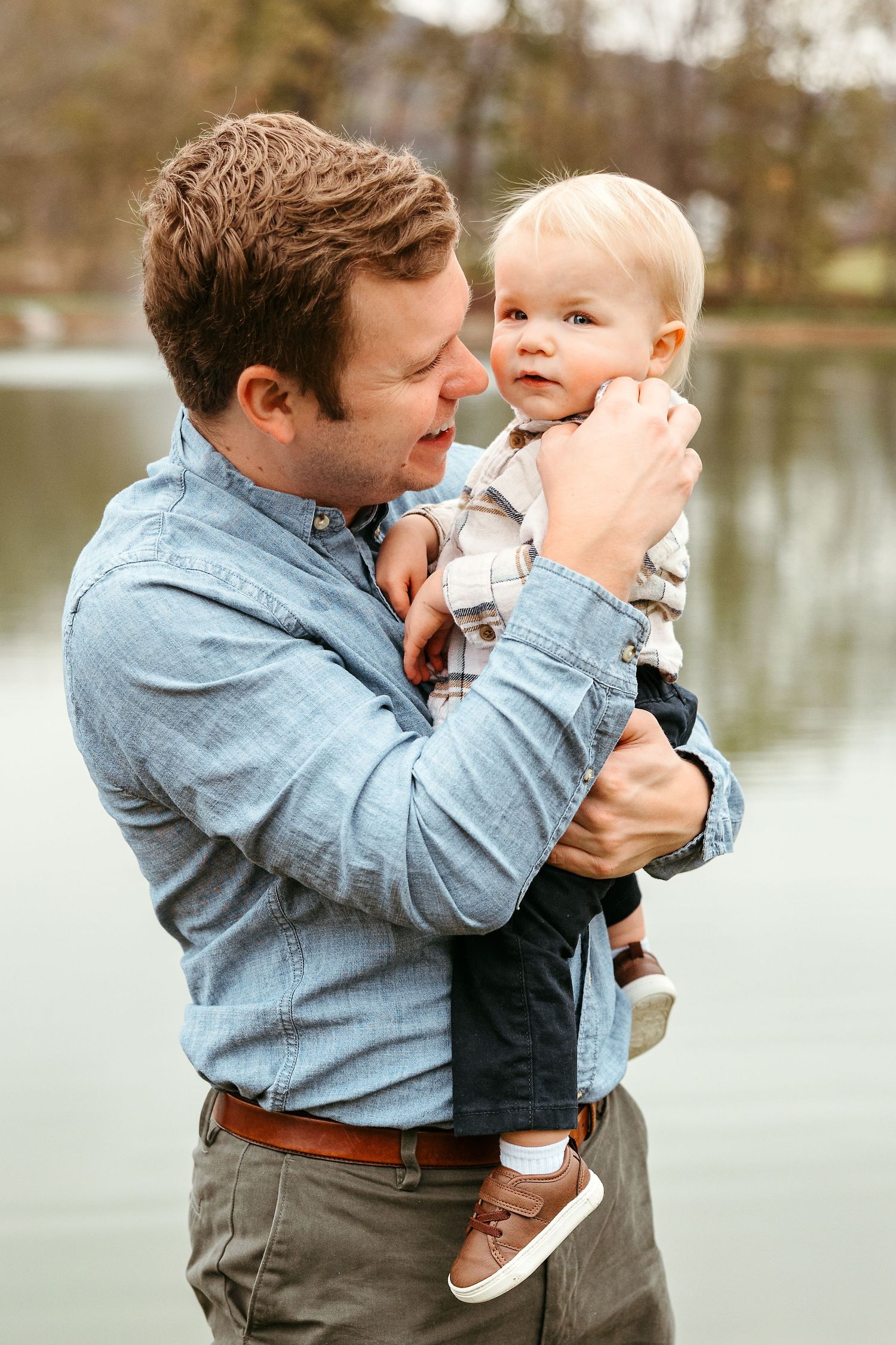 A tender moment between parent and child outdoors by a lake on an autumn day.