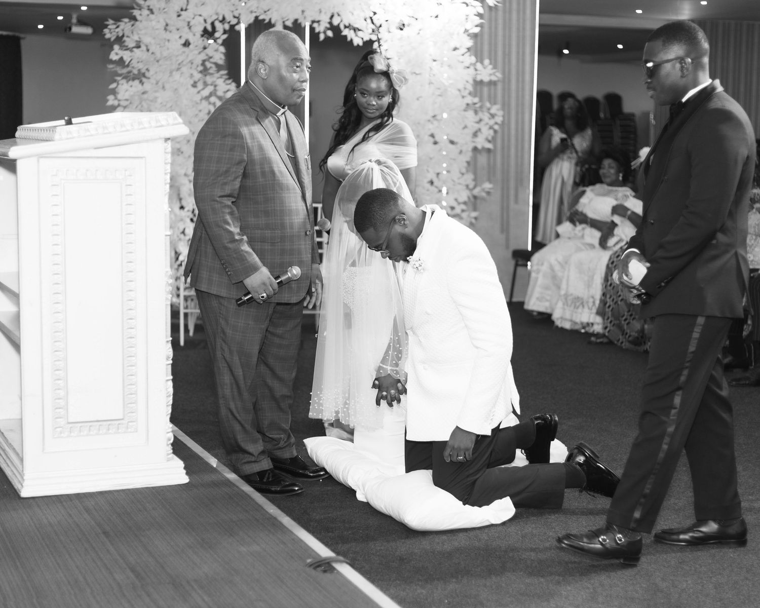 A tender moment during a wedding ceremony as someone kneels before the couple.