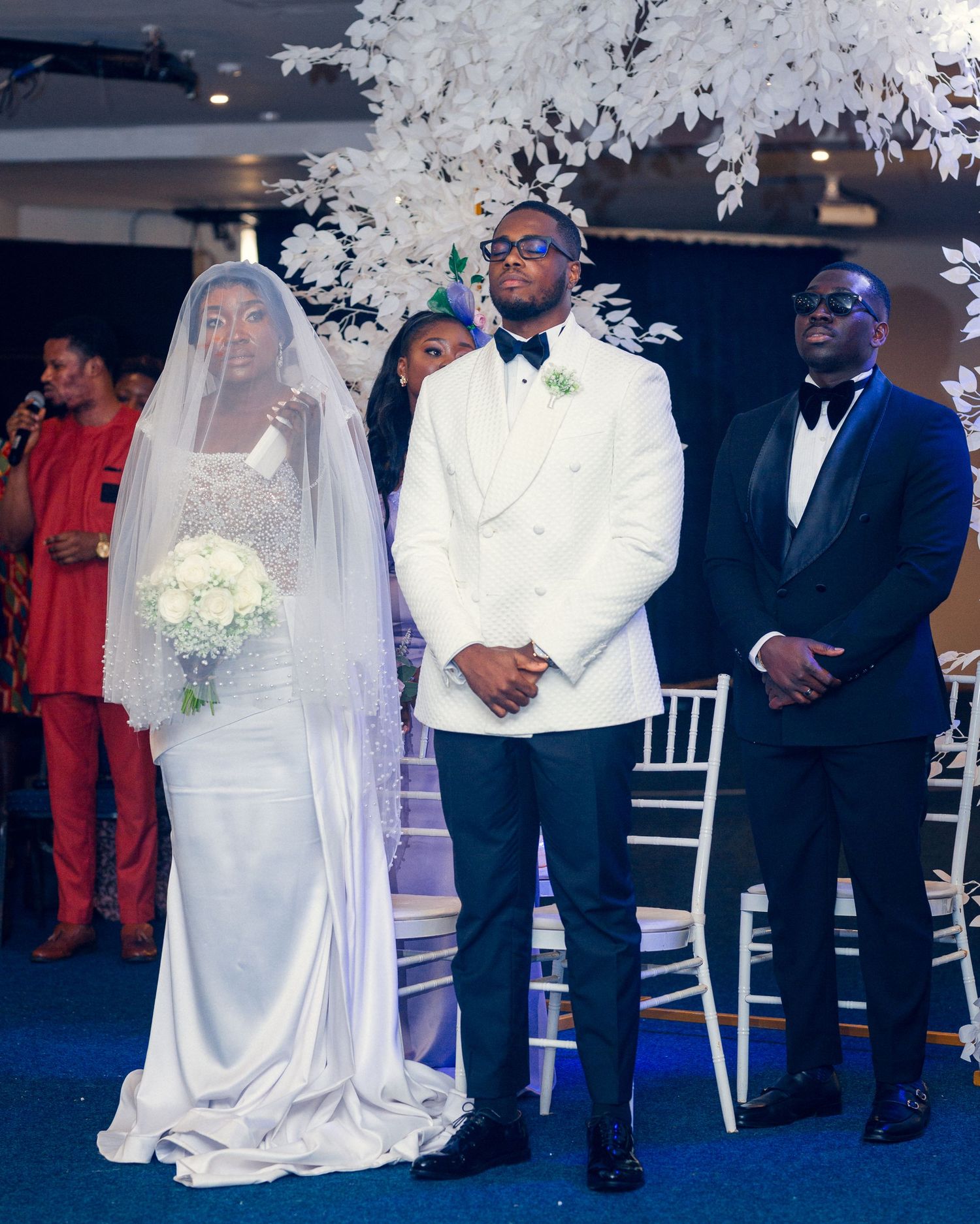 A wedding ceremony scene with white floral decorations and formal attire.