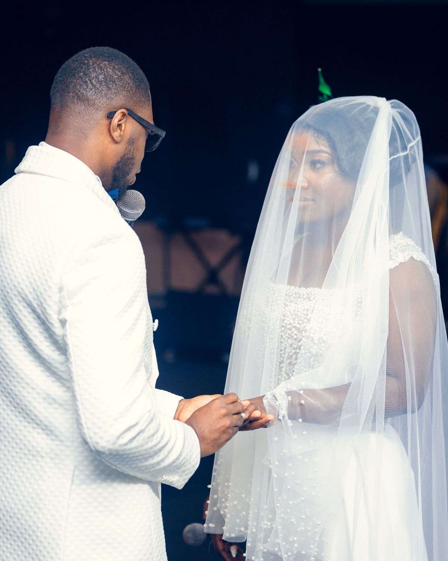 Wedding couple shares intimate ring exchange moment during ceremony, with bride wearing delicate veil.