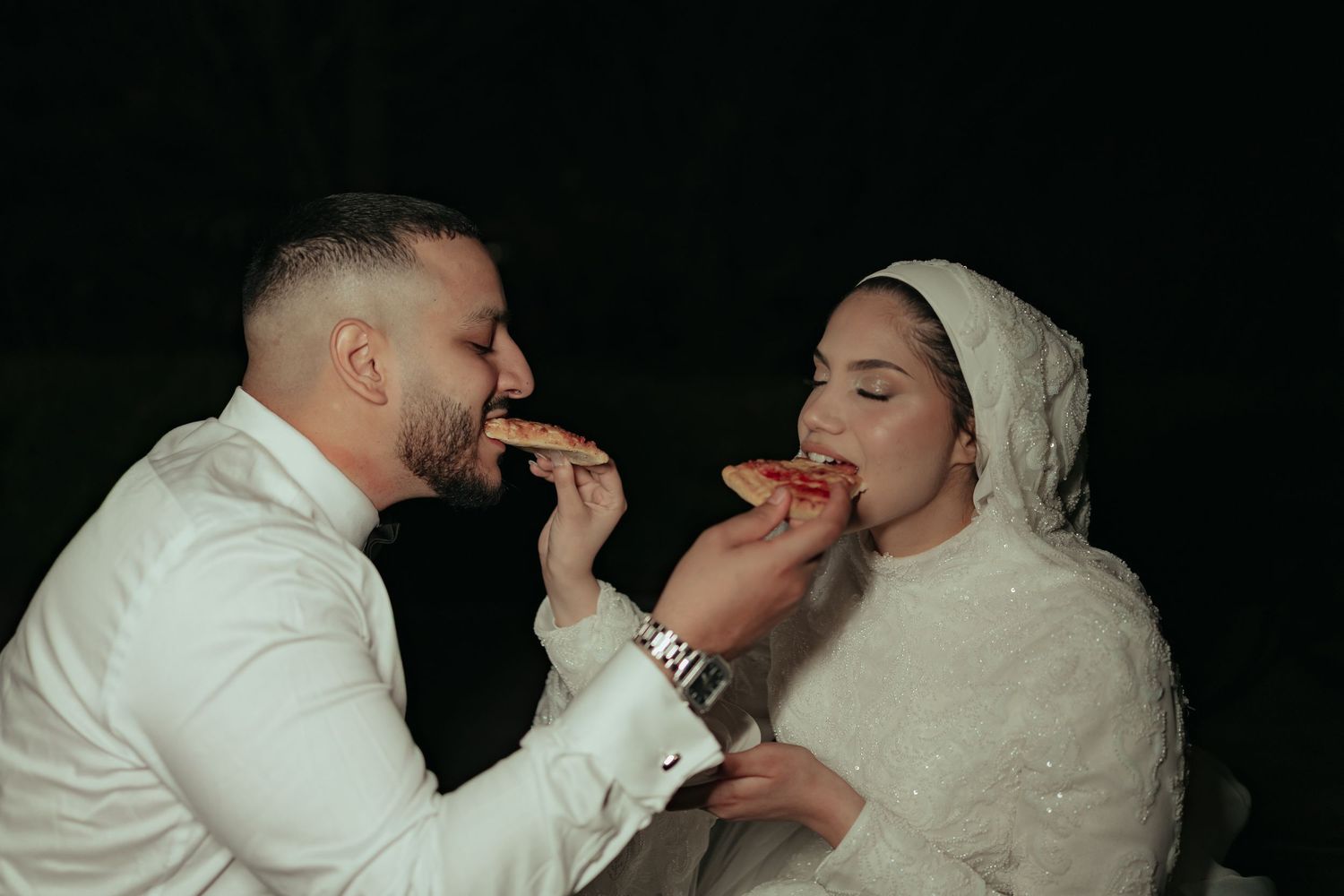 A couple in traditional South Asian wedding attire relaxing on a blanket in a green park.