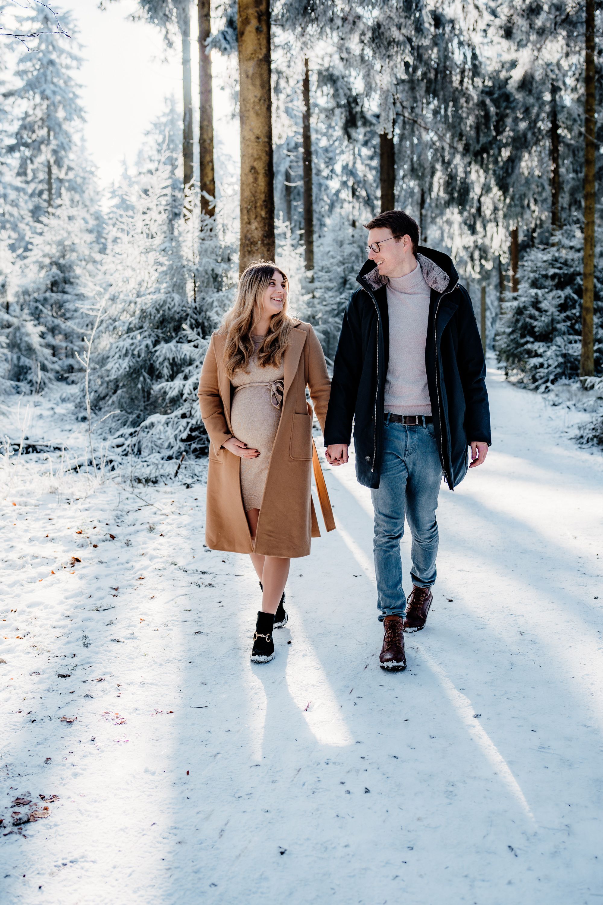 Couple walking hand in hand on a snowy path through a winter wonderland forest scene.