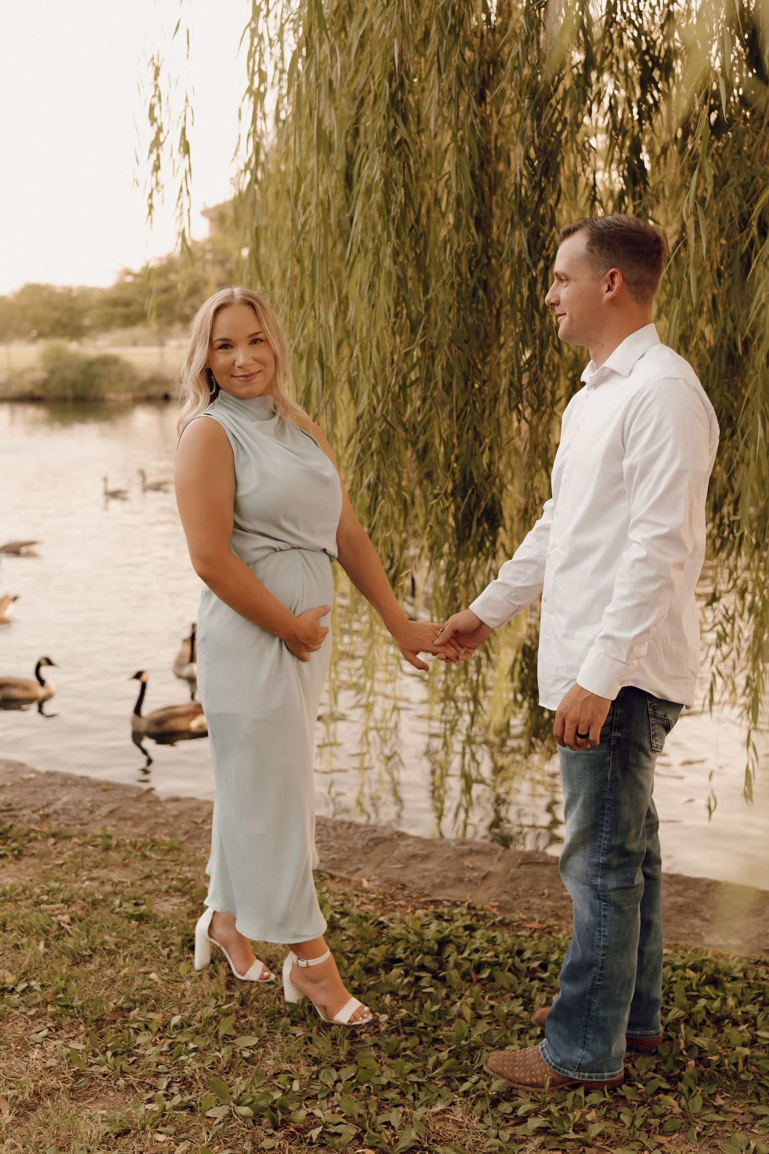 Elegant maternity portrait of a woman with a glowing smile, standing in a scenic outdoor location.