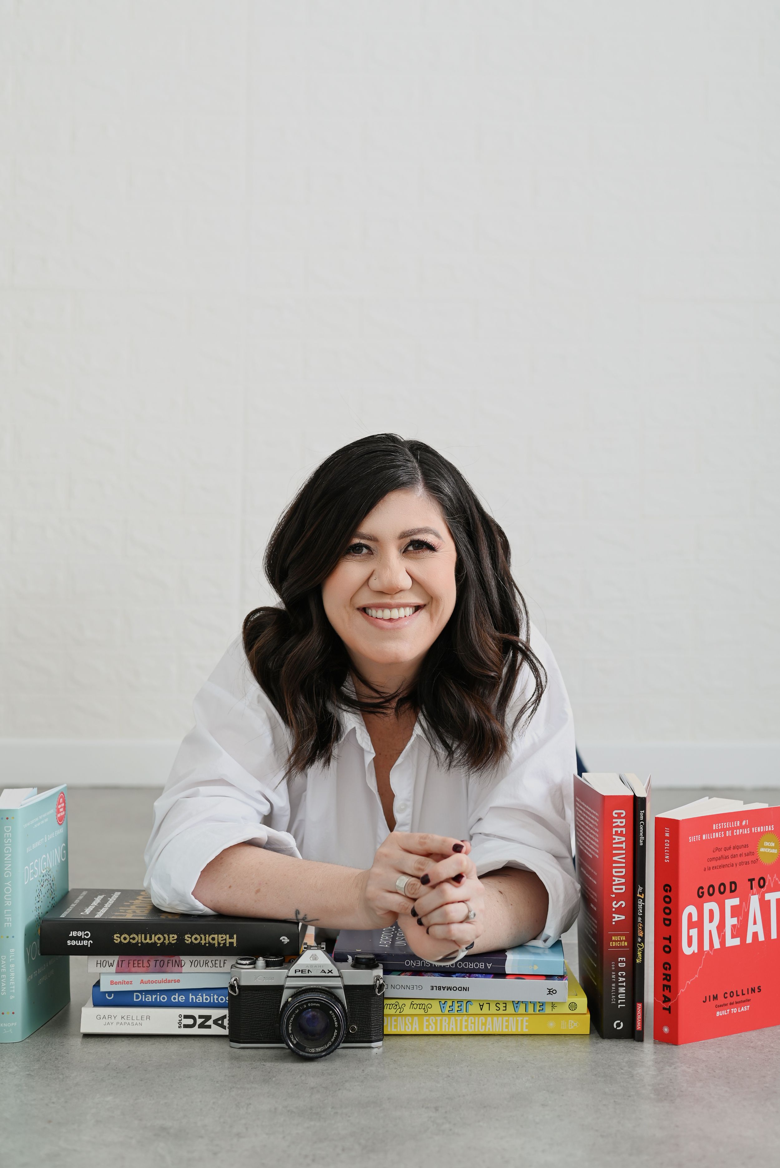 A person in white leans over a table with books and a vintage camera, creating a casual lifestyle scene.
