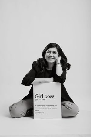 Black and white portrait showing someone sitting cross-legged on floor with 'Girl boss' text display in professional setup.