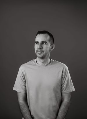 Black and white portrait of a person in a light t-shirt looking off camera against a dark background.
