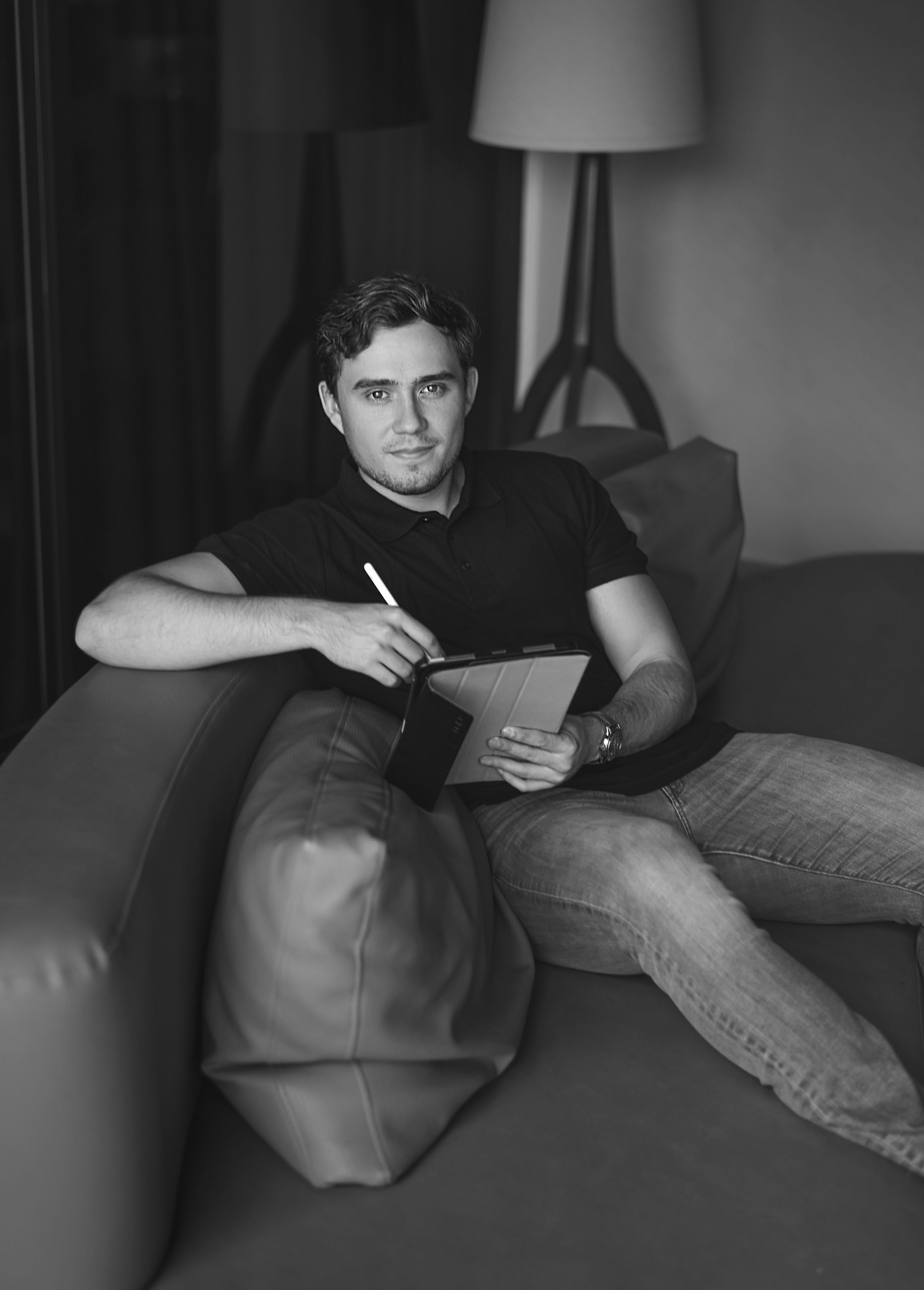 Black and white photo showing someone reclining on a sofa with a notepad while writing, with a lamp in the background.