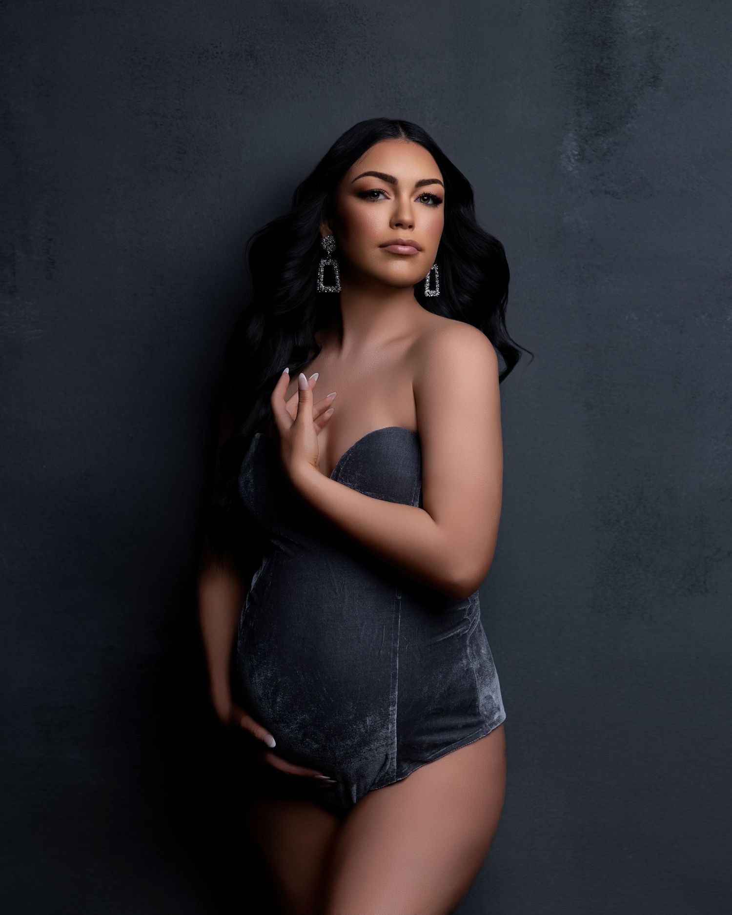 Moody portrait of a woman in a dark velvet bodysuit against a textured grey background.