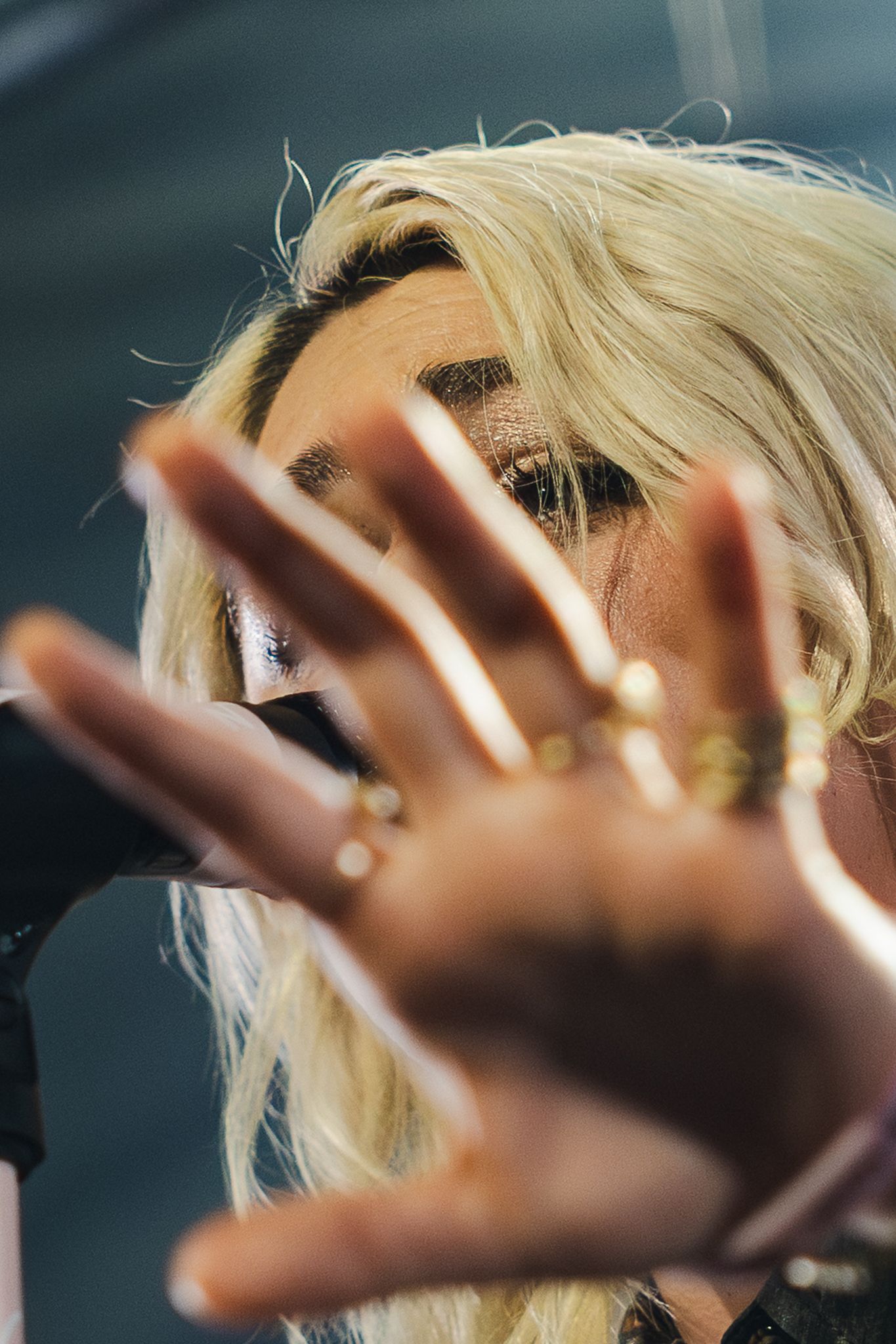 Blonde woman holding hand up to camera wearing gold rings, artistic close-up portrait shot.