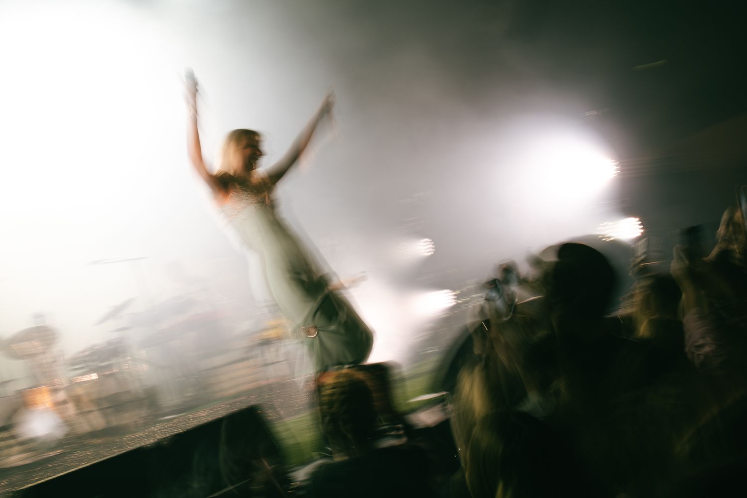 Blurry motion shot of a crowd at an energetic concert with dramatic lighting and fog effects.
