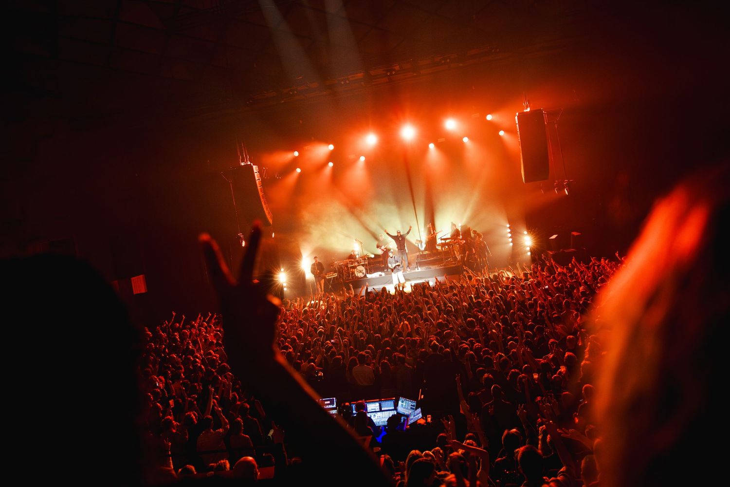 Concert crowd silhouettes against bright red stage lights during a live performance at a packed music venue.