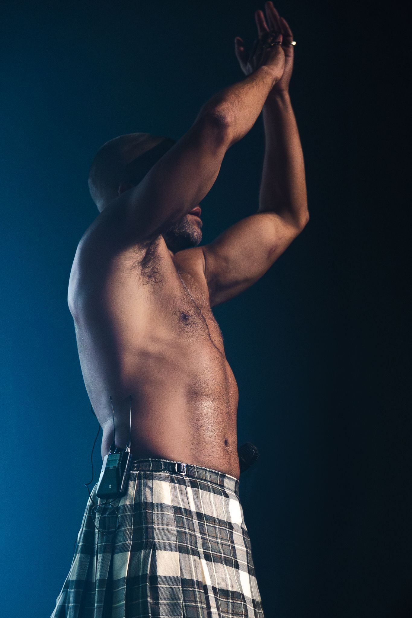 Artistic photo series showing torso in plaid shorts against dark blue background with dramatic lighting.