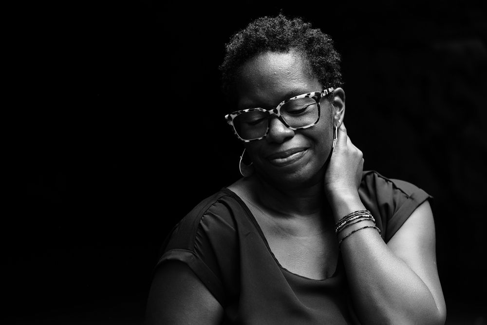Black and white portrait of someone wearing glasses against dark background with a warm expression.