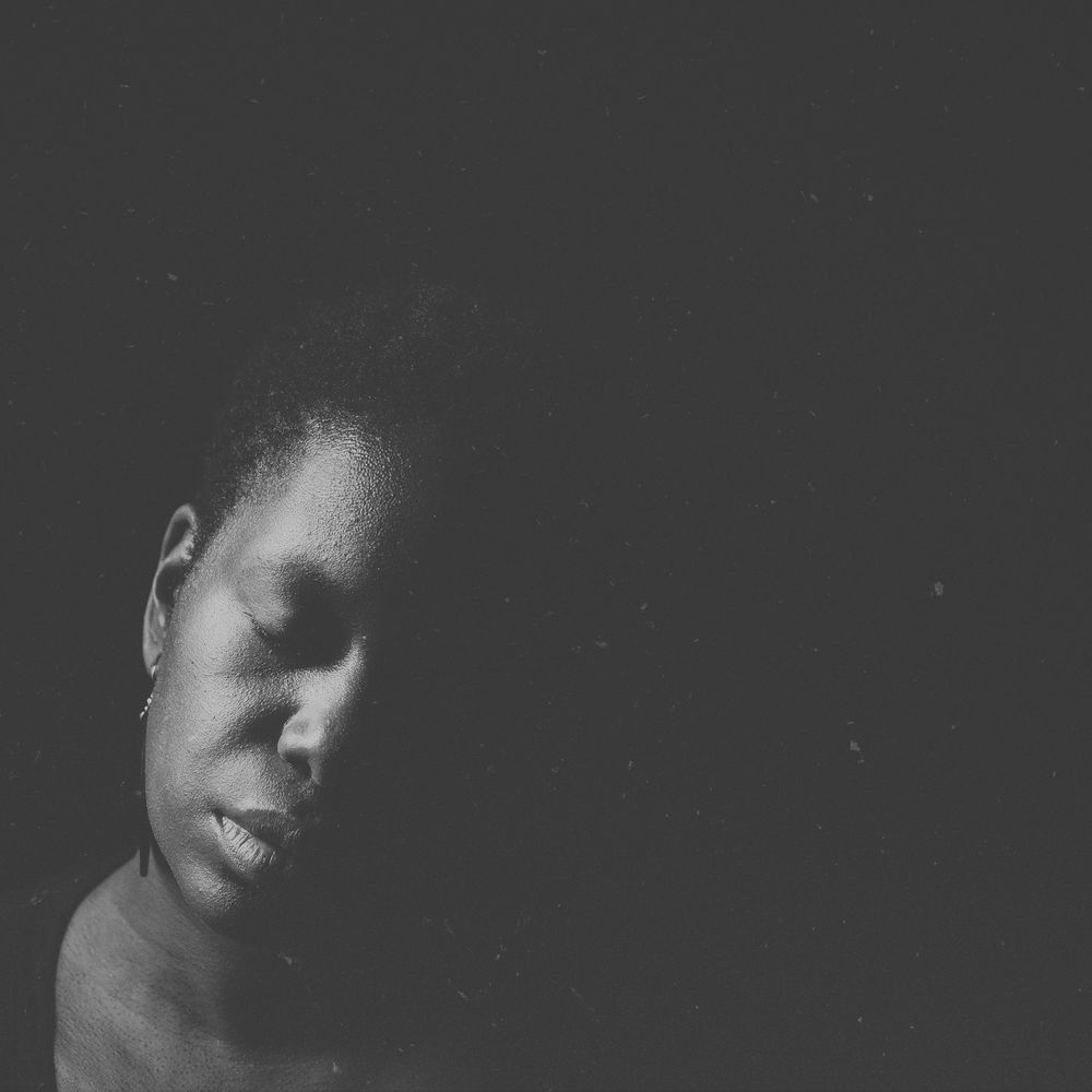 Artistic black and white portrait in low light showing a face in profile against a dark background.