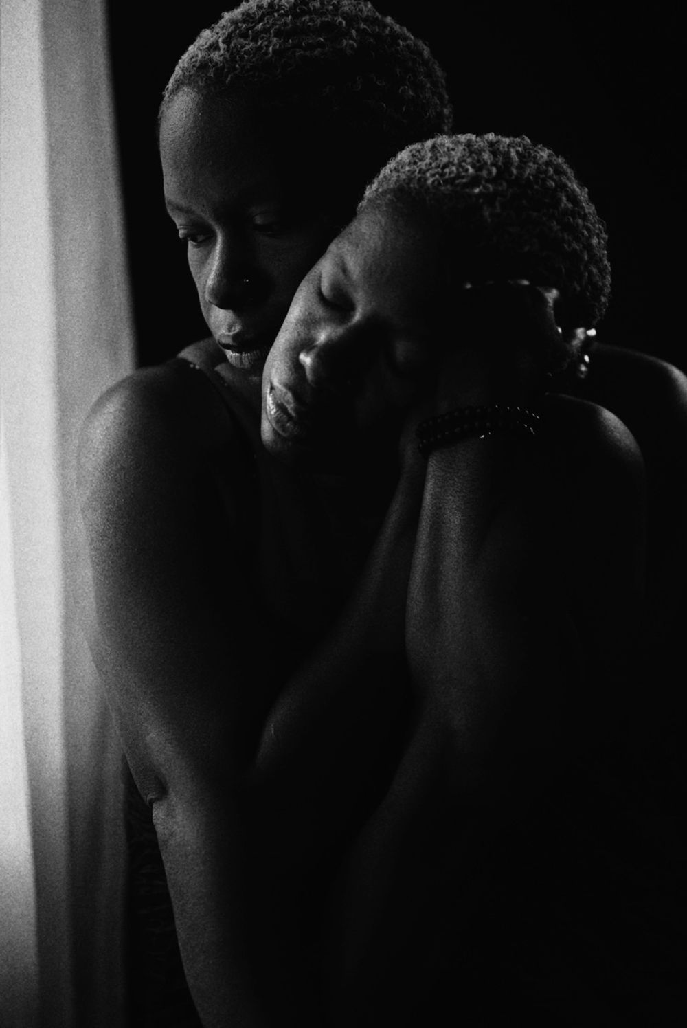 Dramatic black and white portrait showing intimate shadowed silhouettes near a window in low key lighting.