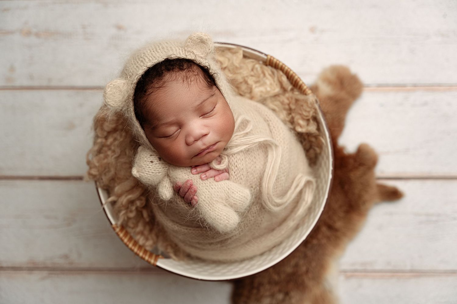 Peaceful newborn baby wearing floral headband wrapped in cream fabric on fuzzy backdrop.