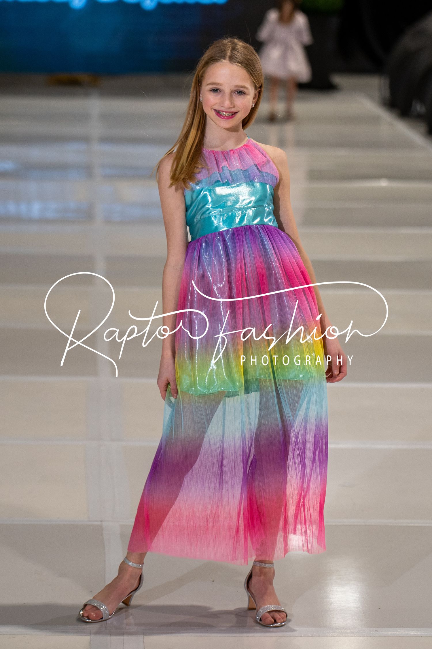 Model walks the runway in a colorful rainbow tie-dye maxi dress at a fashion show event.