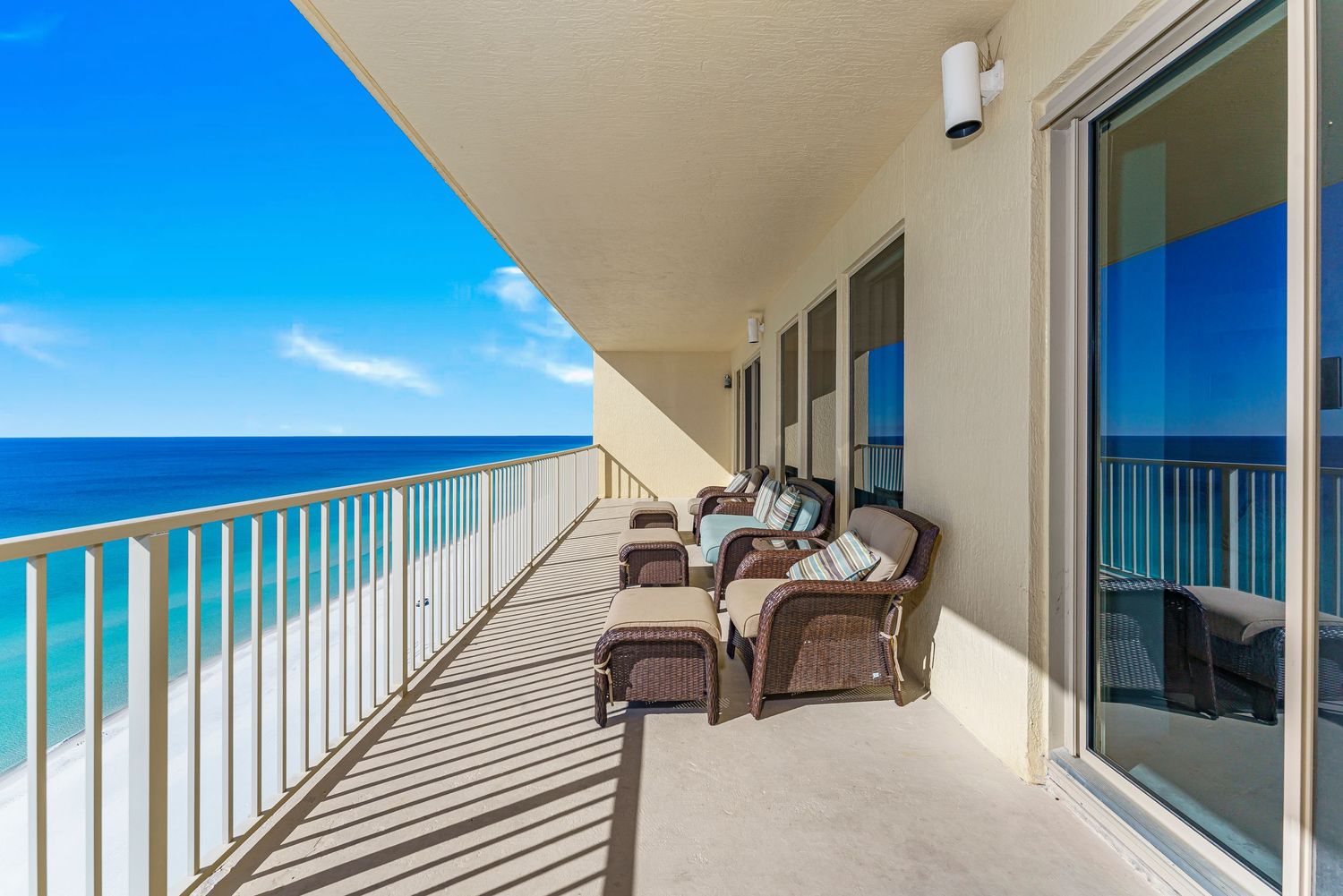Beachfront balcony with wicker chairs overlooking turquoise ocean waters and white sand beach under blue skies.