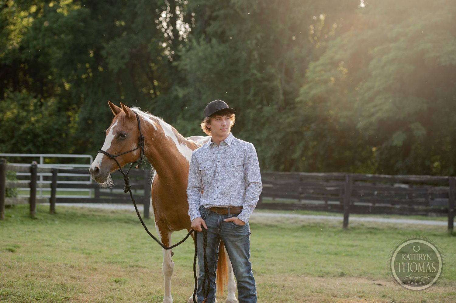 Brown and white horse poses with rider near wooden fence during sunset.