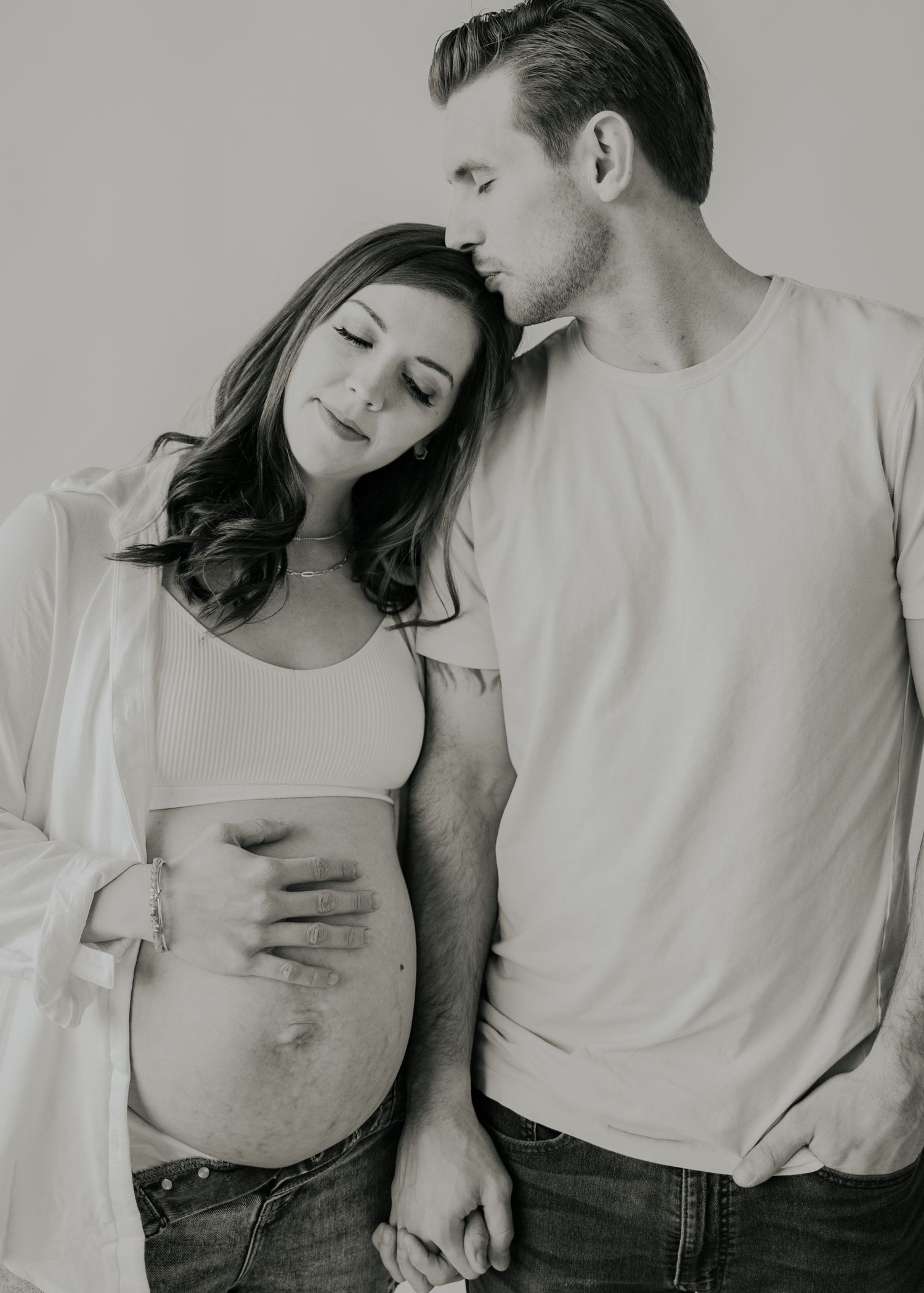 Black and white maternity photo of a couple in casual clothing sharing an intimate moment together.