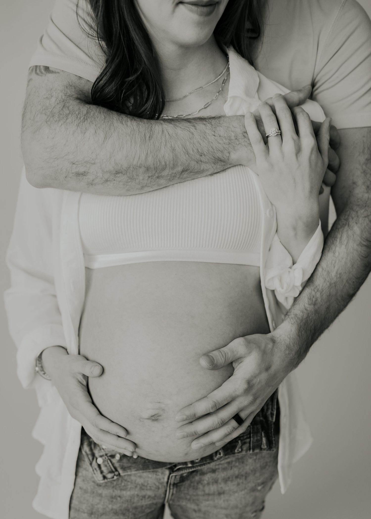 Black and white intimate maternity photo showing a couple embracing with hands resting on pregnant belly.