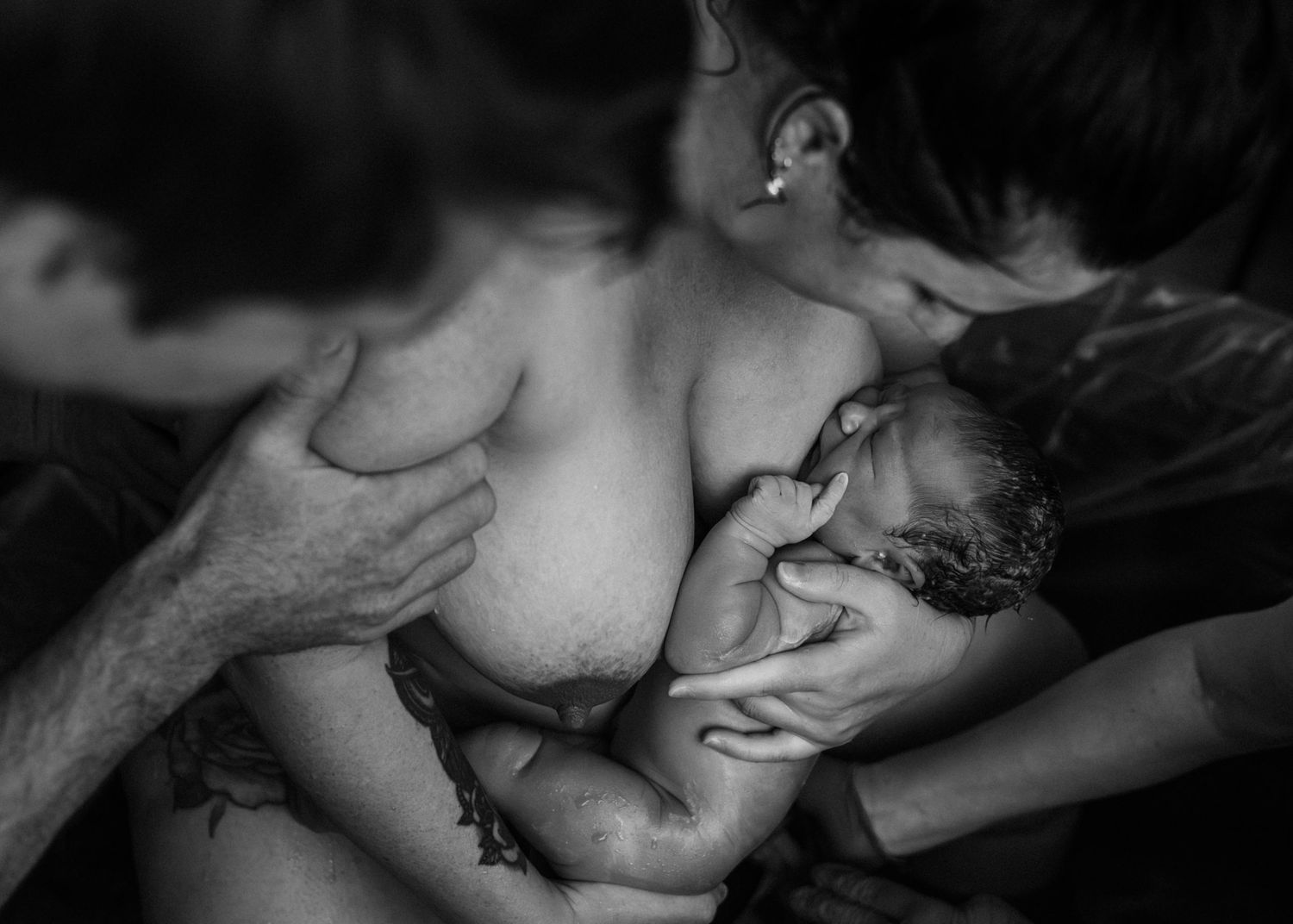 A newborn baby sleeps peacefully while being cradled against bare skin in intimate skin-to-skin contact.