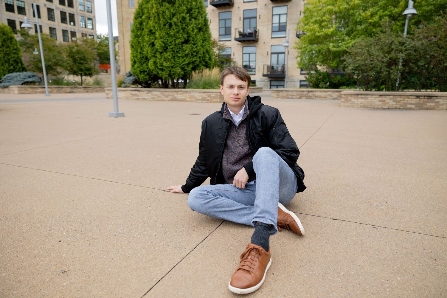 A casual portrait on concrete ground with urban architecture in background.