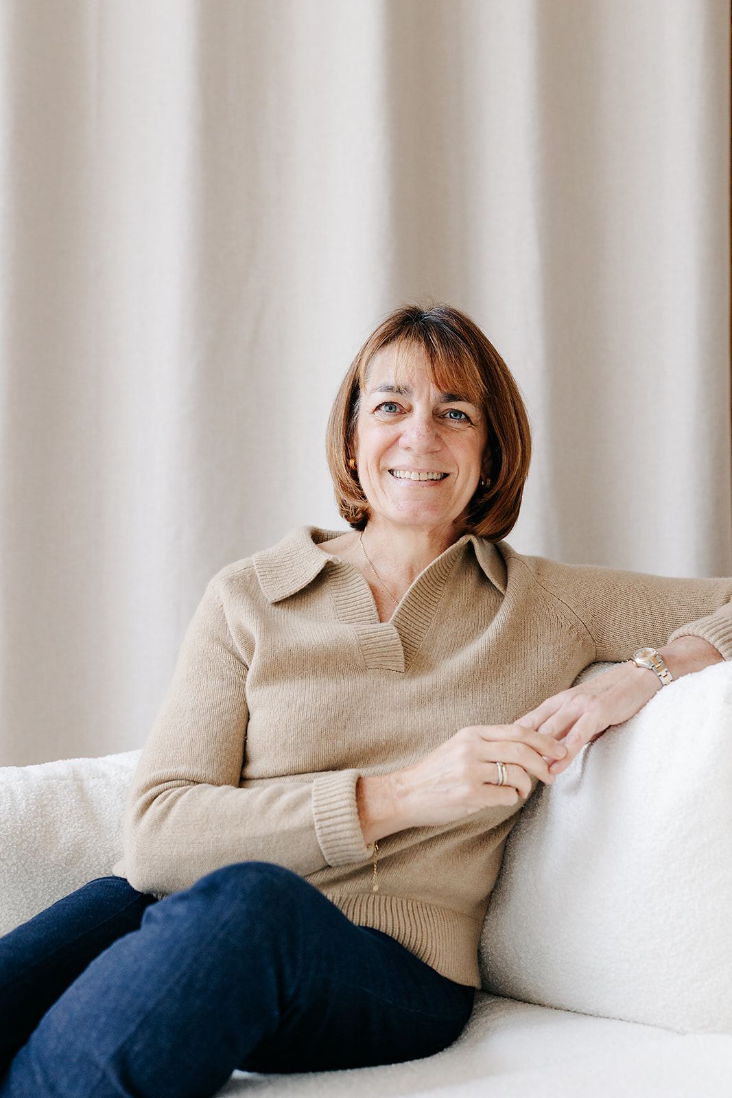 Person in beige sweater and jeans relaxes on white couch in sequence of casual lounging poses. Hampshire Headshot photography