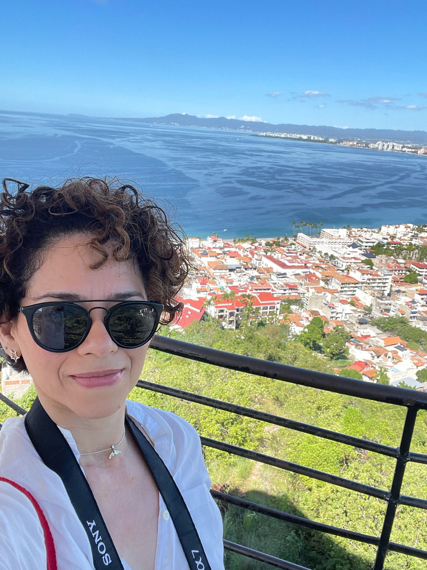 A scenic selfie overlooking a coastal city with blue water and mountains in the background.