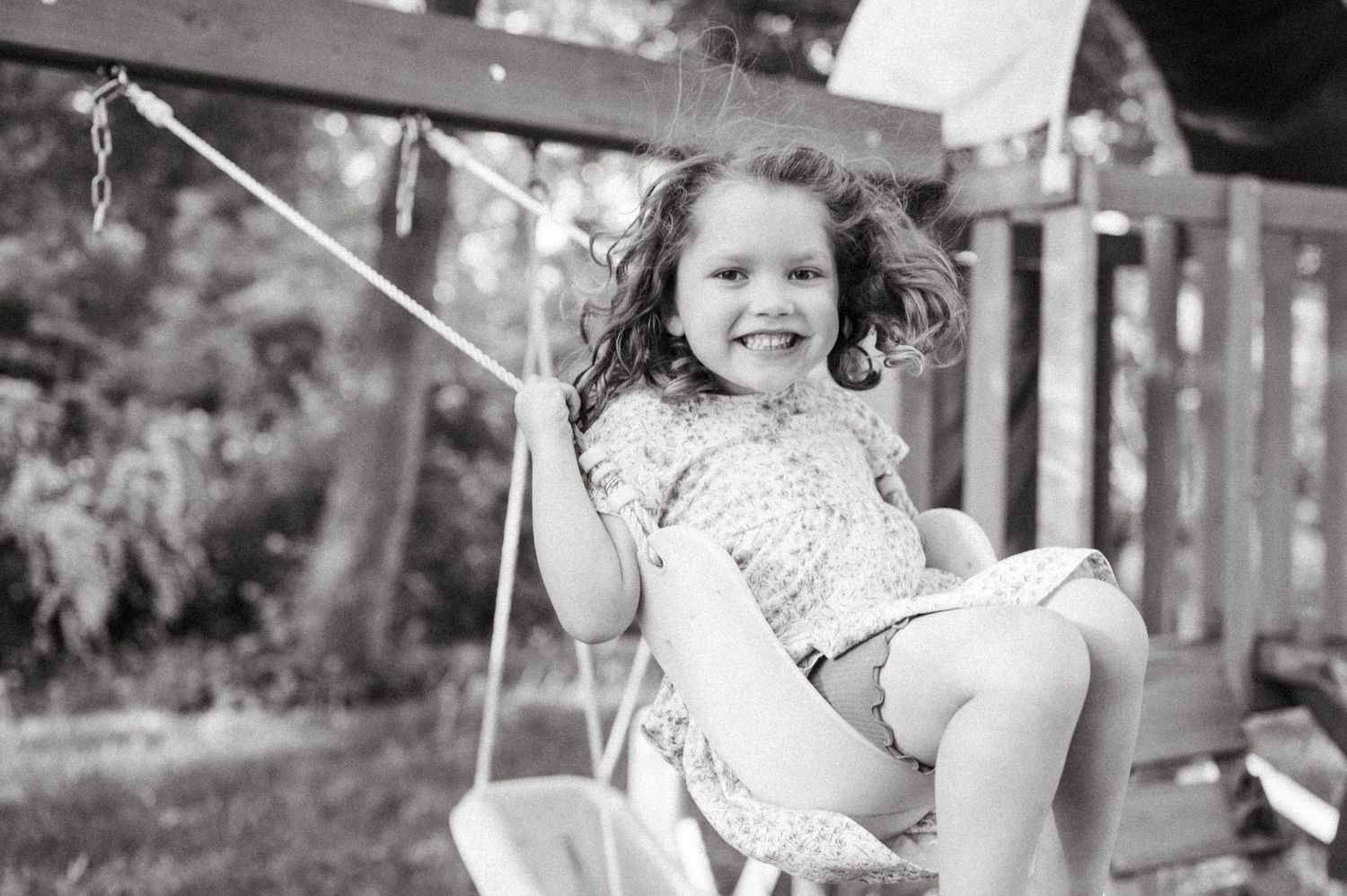 Black and white photo of young girl joyfully swinging outdoors.