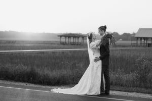 A romantic black and white wedding photo of a couple embracing on a country road at sunset with palm trees in the distance.