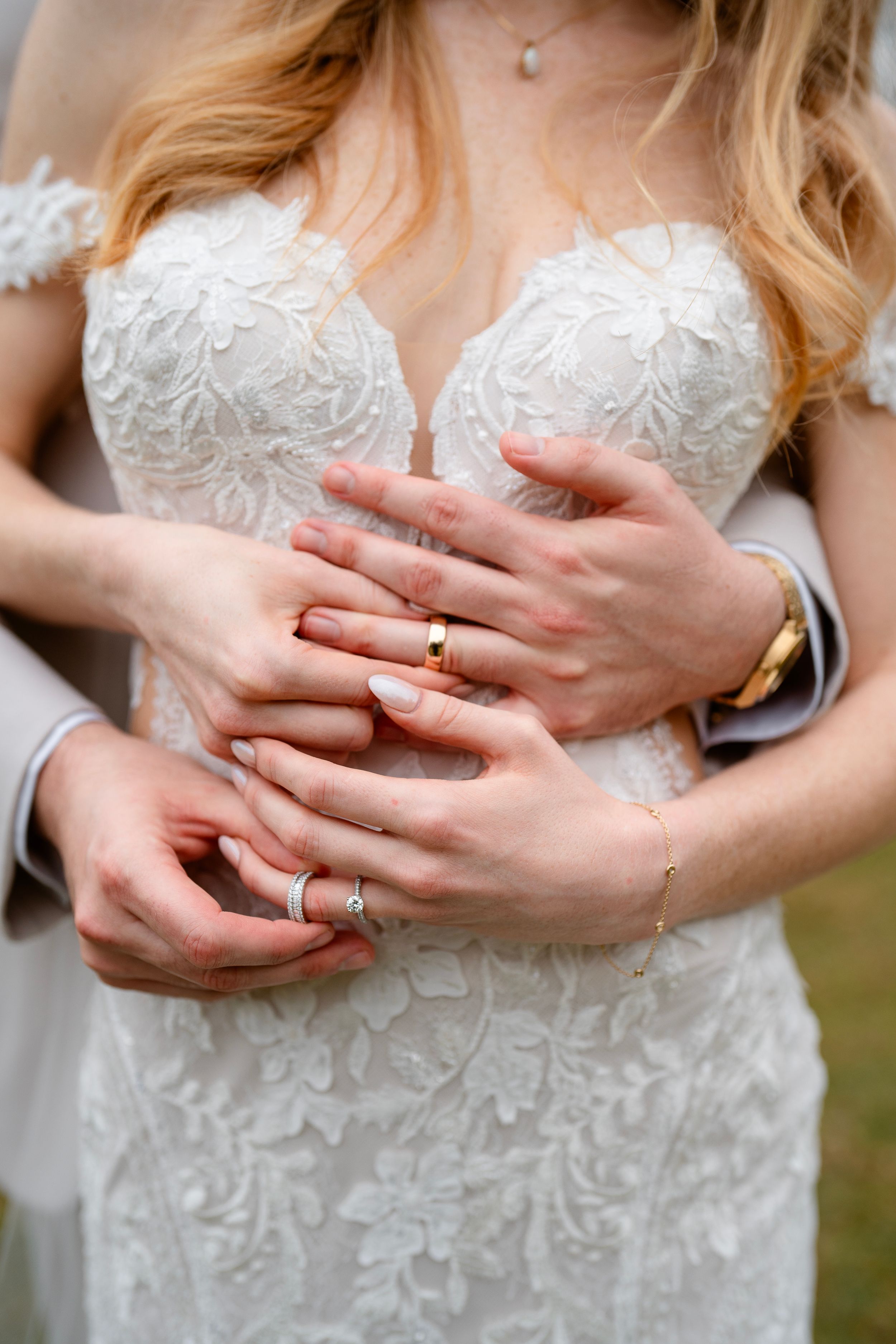 Close up of hands with wedding rings against an ornate white lace wedding dress bodice.