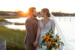 A romantic newlywed couple shares an intimate moment at sunset by a marsh with a vibrant sunflower bouquet.