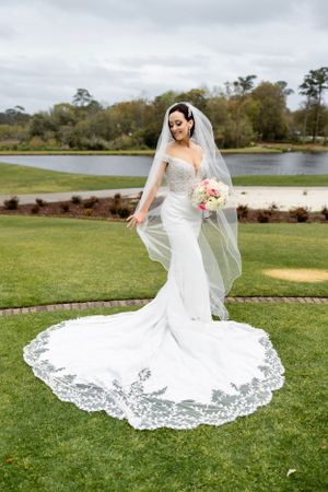 A stunning wedding dress with beautiful lace train displayed on manicured golf course lawn beside a pond.
