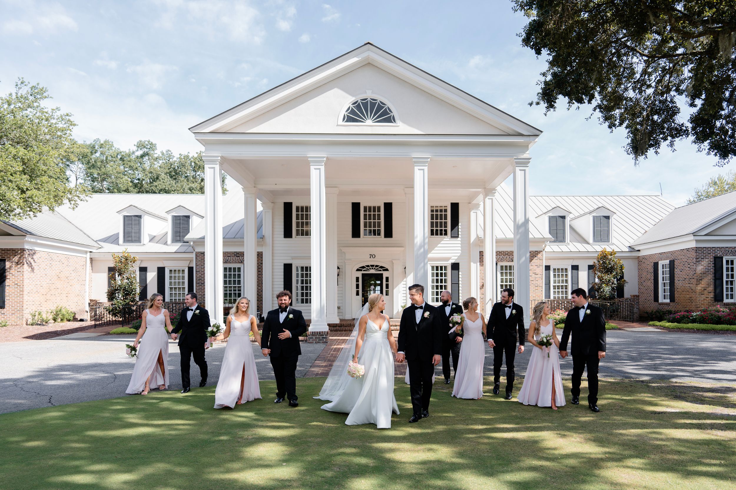 Wedding party gathered in front of a grand Southern plantation-style home with white columns.