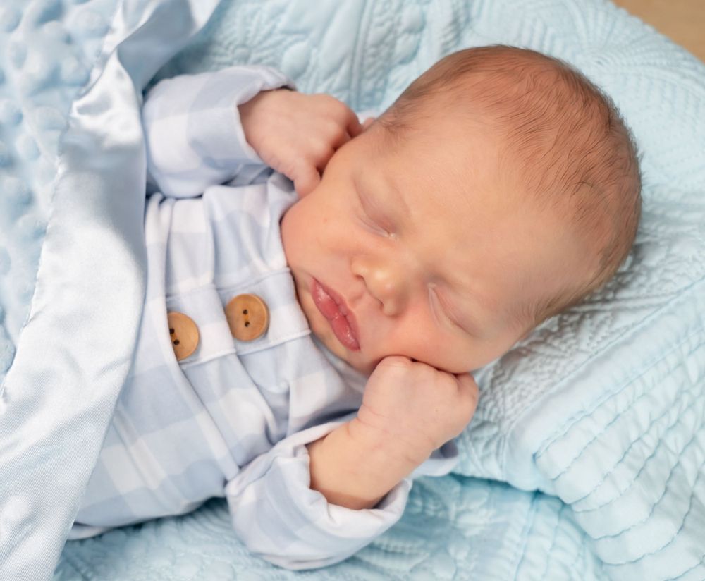 Newborn baby sleeping peacefully on light blue quilted bedding.