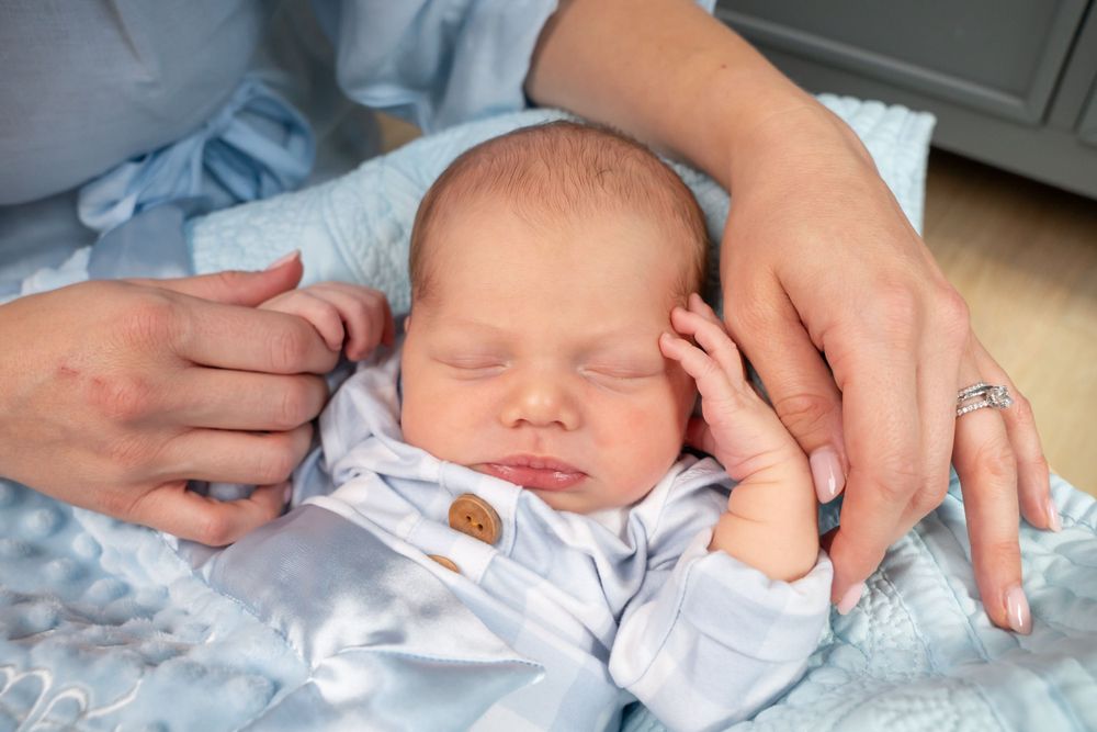 Closeup of tiny newborn hands reaching out while wearing a light blue outfit.