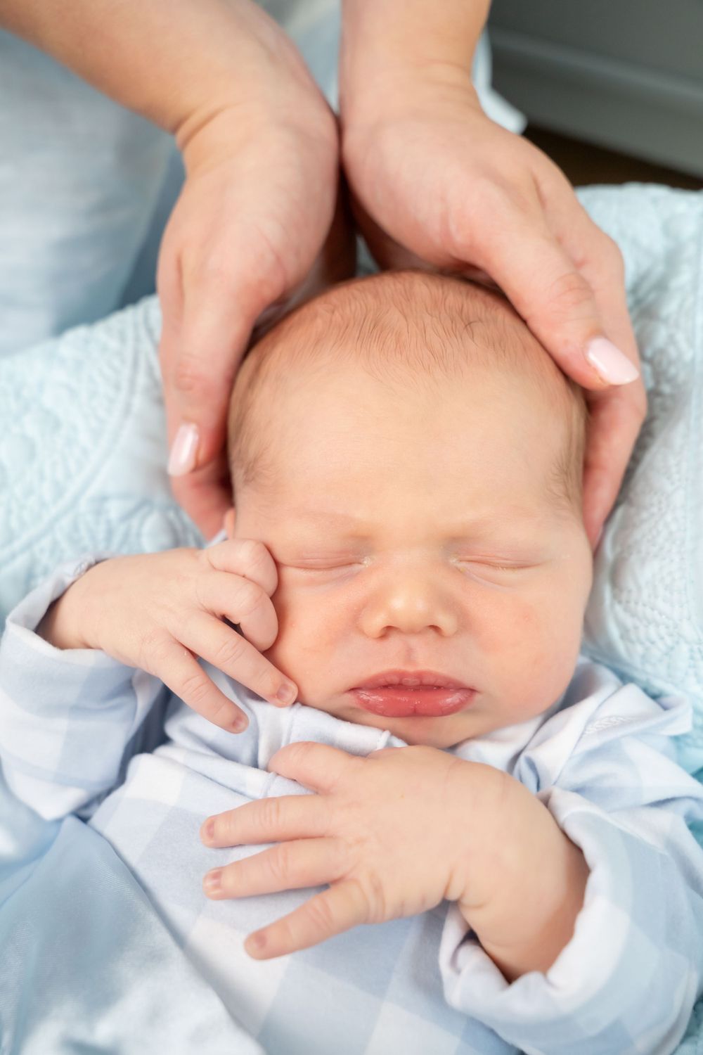 Peaceful sleeping newborn in light blue clothing with adult hands gently cradling.