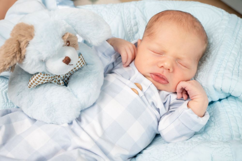 Sleeping infant wearing light blue outfit resting on white blanket.